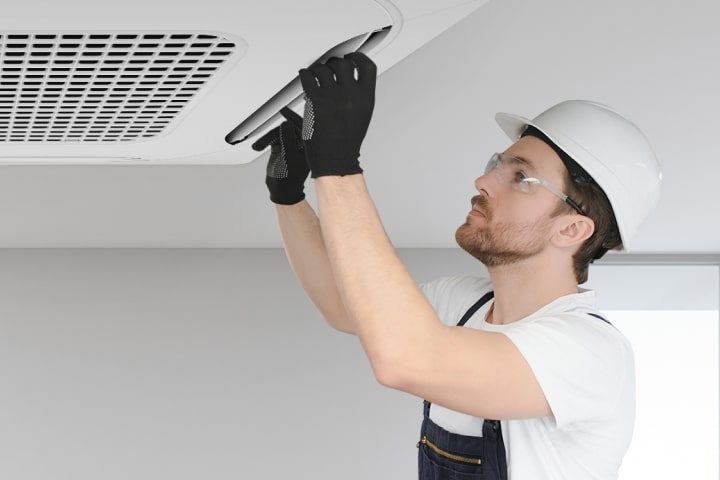 فني يركّب وحدة تكييف الهواء LG ceiling-mounted cassette أو يقوم بصيانتها، مرتديًا ملابس السلامة.